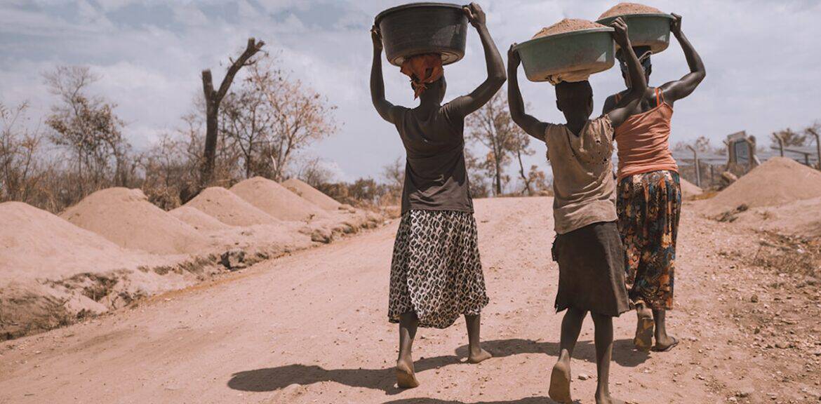 Mujeres cargando canastos sobre sus cabezas en camino de tierra.