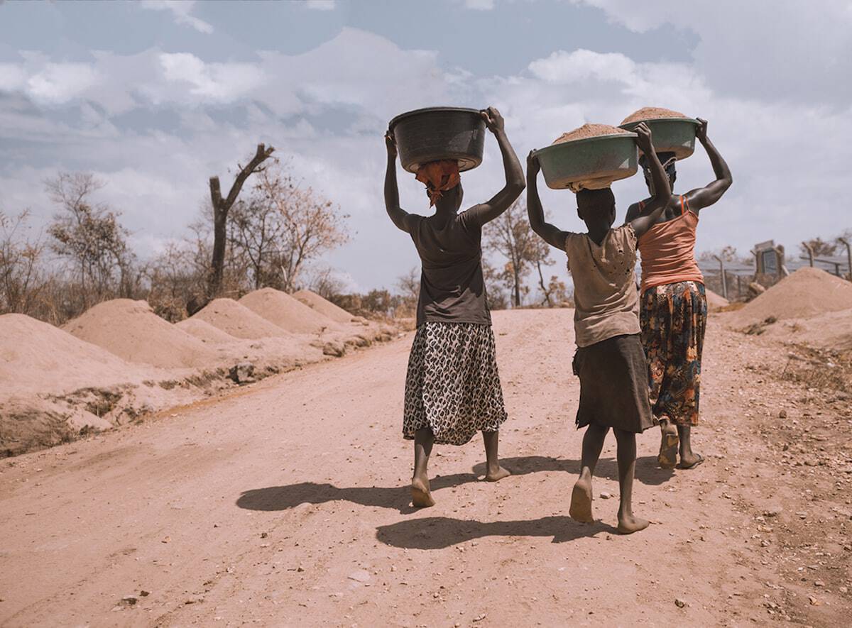 Mujeres cargando canastos sobre sus cabezas en camino de tierra.